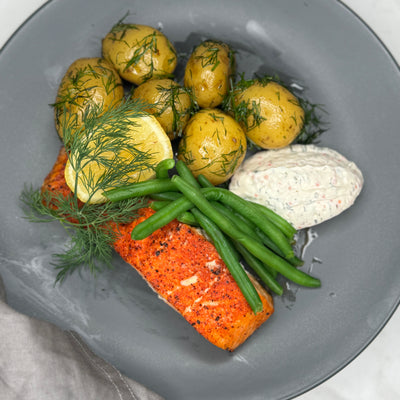 Grillad lax ligger på en tallrik som ett serveringsförslag. Tillsammans med kokt potatis, citron och romsås.