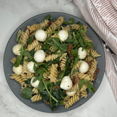 Pasta Pesto ligger på en tallrik som ett serveringsförslag. Man ser innehållet såsom pasta, mozzarellakulor och ruccola