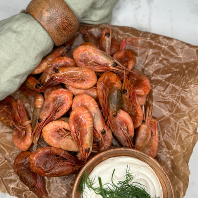 Rökta räkor ligger utspritt på vaxad bakplåtspapper som ett serveringsförslag tillsammans med en skål aioli.