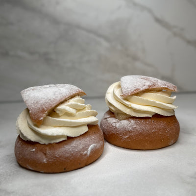 Vetesemla fotad från sidan där man ser spritsad grädde, mandelmassa och locket toppad med florsocker.