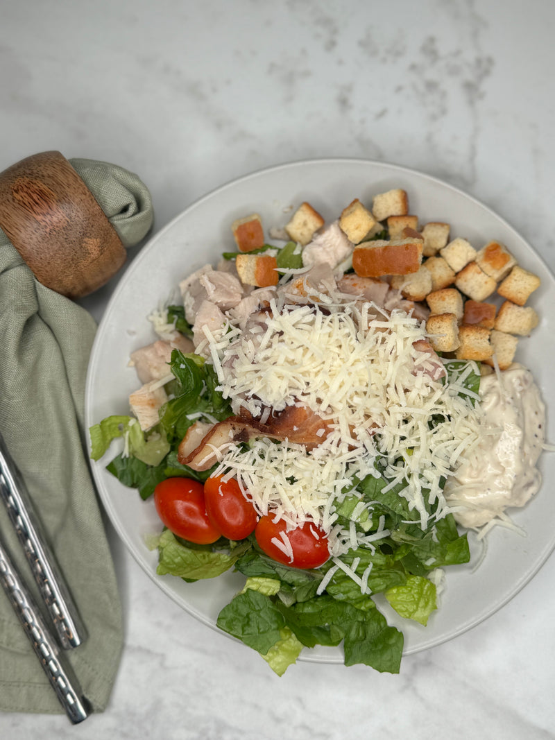 Ceasarsallad med kyckling upplagd på en tallrik som ett serveringsförslag. Fotad ovanifrån 