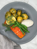 Grillad lax ligger på en tallrik som ett serveringsförslag. Tillsammans med kokt potatis, citron och romsås.