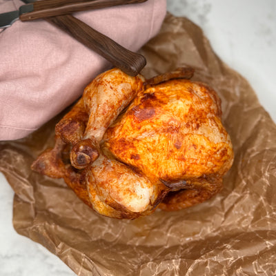 En hel grillad kyckling fotad ovanifrån, ligger på ett vaxat bakplåtspapper