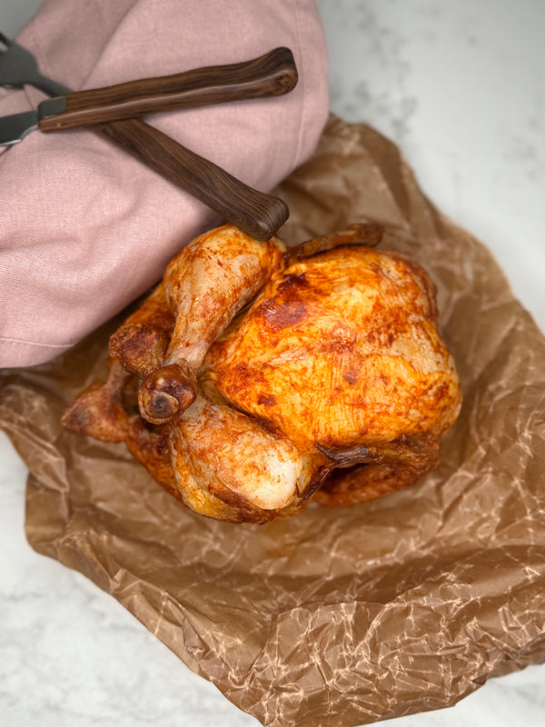 En hel grillad kyckling fotad ovanifrån, ligger på ett vaxat bakplåtspapper