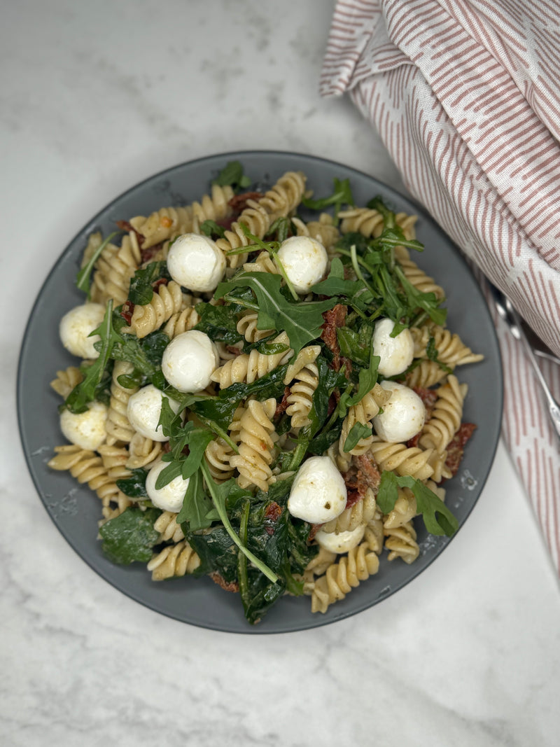 Pasta Pesto ligger på en tallrik som ett serveringsförslag. Man ser innehållet såsom pasta, mozzarellakulor och ruccola