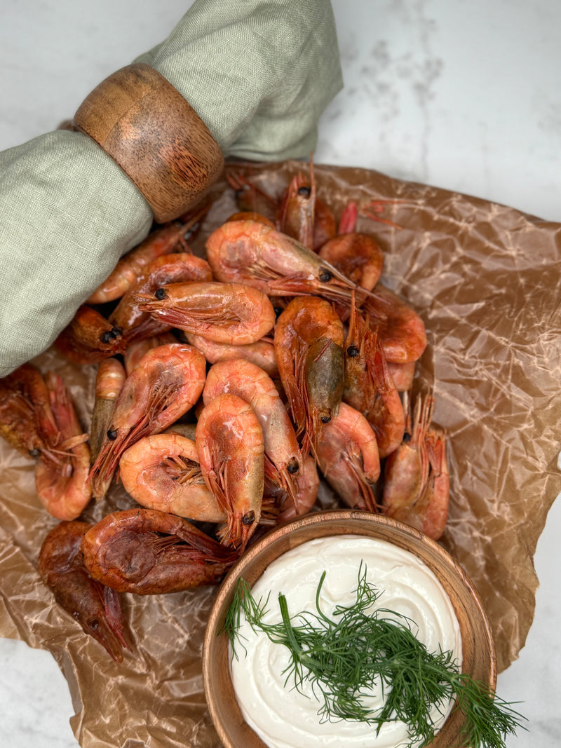 Rökta räkor ligger utspritt på vaxad bakplåtspapper som ett serveringsförslag tillsammans med en skål aioli.