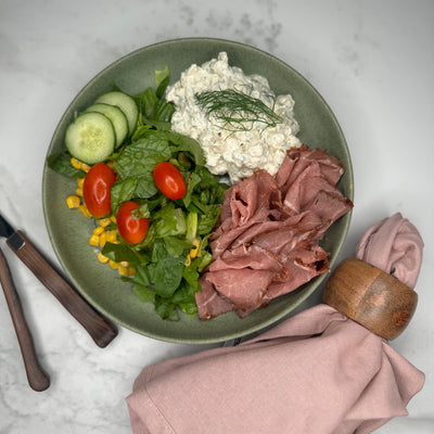 Rostbiff med potatissallad upplagd på en tallrik som ett serveringsförslag tillsammans med en sallad där man ser gurka och tomat.