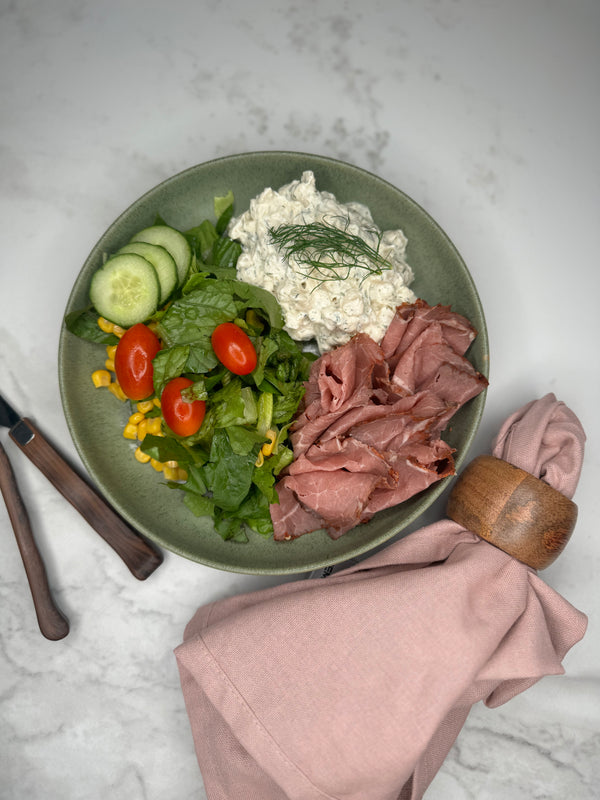 Rostbiff med potatissallad upplagd på en tallrik som ett serveringsförslag tillsammans med en sallad där man ser gurka och tomat.