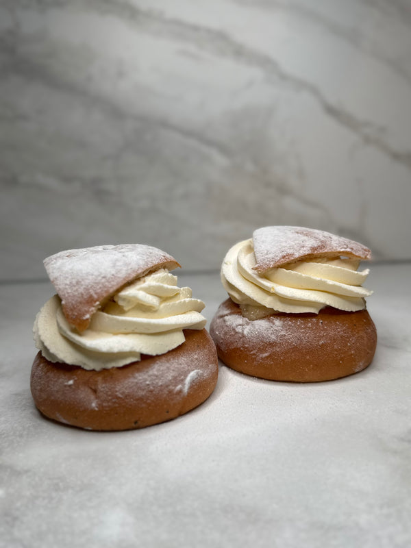 Vetesemla fotad från sidan där man ser spritsad grädde, mandelmassa och locket toppad med florsocker.